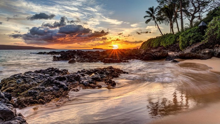 Sunset over a rocky beach with palm trees