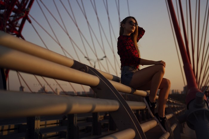 Woman in sunglasses and jean shorts sitting on a bridge