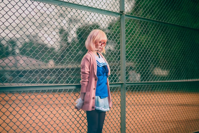 Cosplayer in pink cardigan and blue uniform by fence