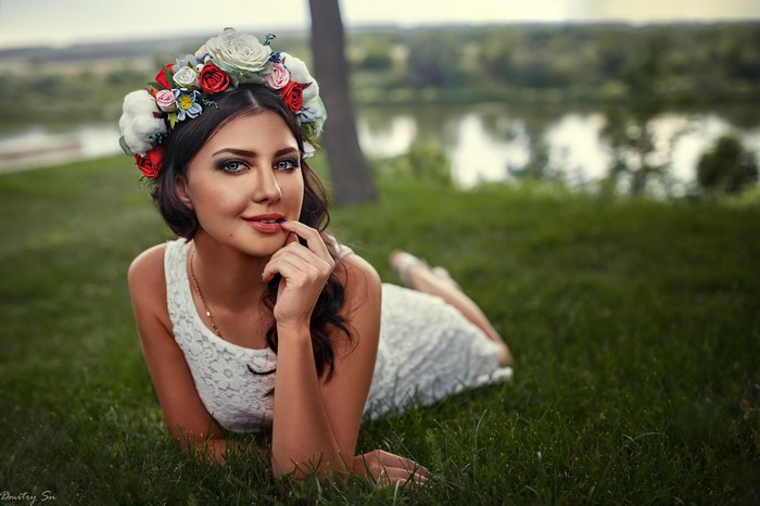 Woman with flower crown lying on grass by river