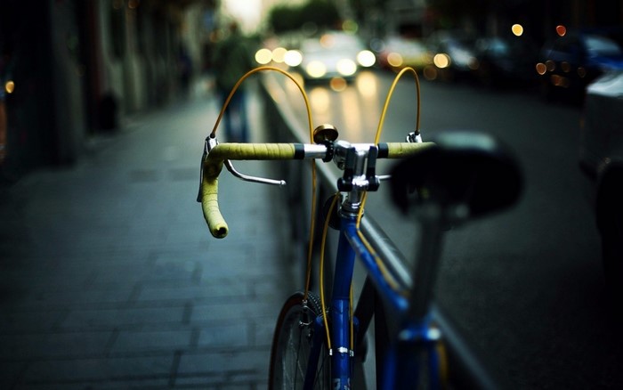 Blue bicycle handlebars with yellow tape on a street