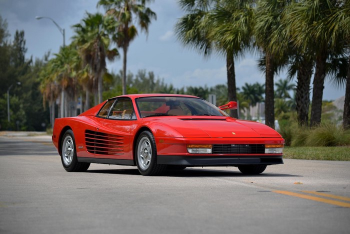 Red Ferrari Testarossa driving on a road with palm trees