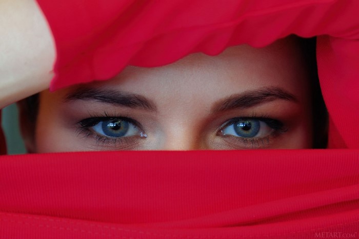 Close up of a woman's blue eyes behind red fabric