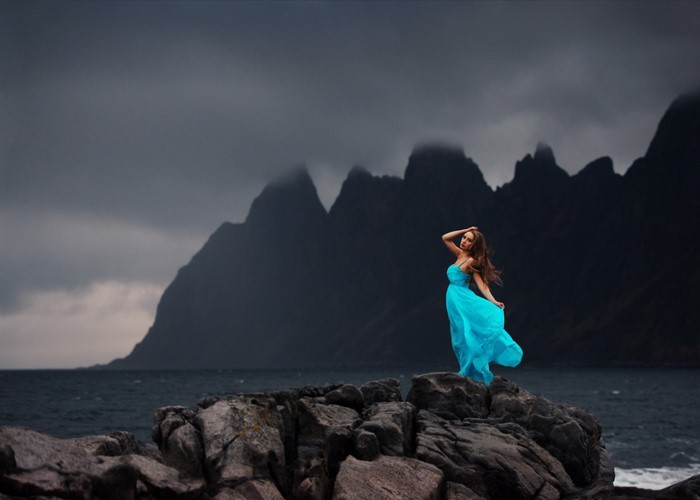 Woman in blue dress on rocks with mountains and sea