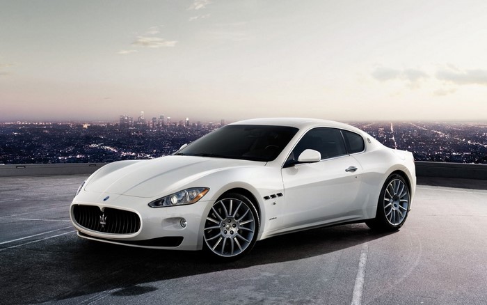 White Maserati GranTurismo parked with city skyline at dusk
