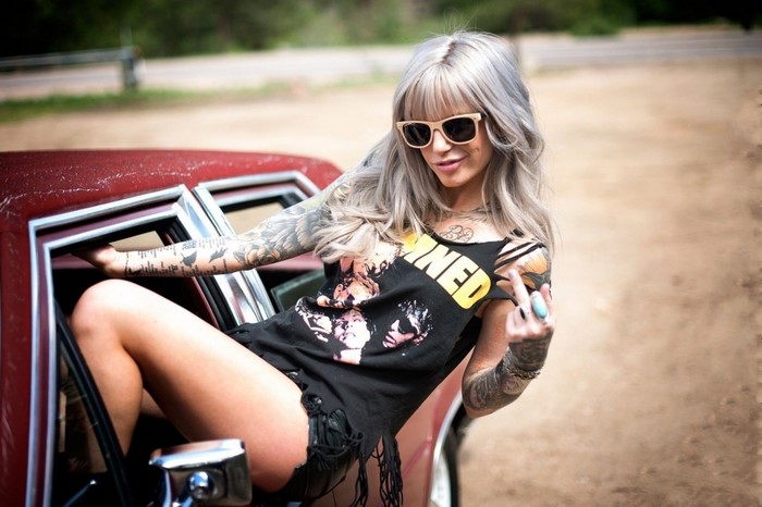 Woman with tattoos and sunglasses leaning on a red car