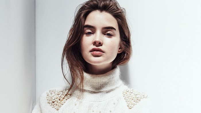 Woman with long brown hair wearing a pearl-adorned sweater