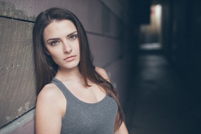 Woman with long brown hair leaning against a wall