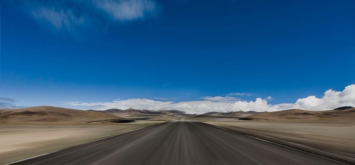 Road through a vast, arid landscape under a blue sky