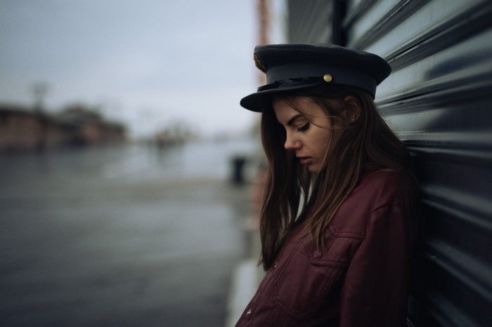 Woman wearing a cap and jacket leaning against a wall