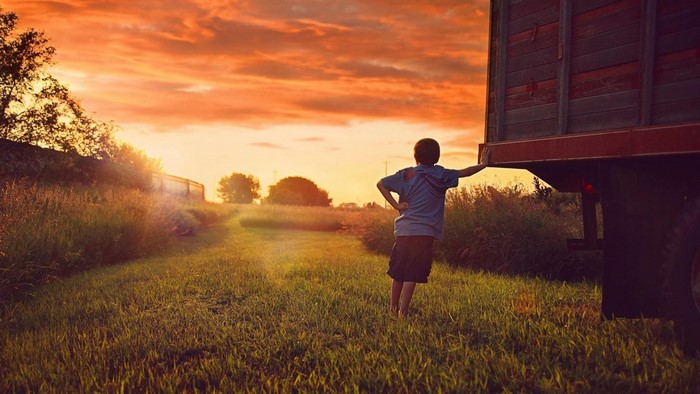 Boy leaning on truck at sunset