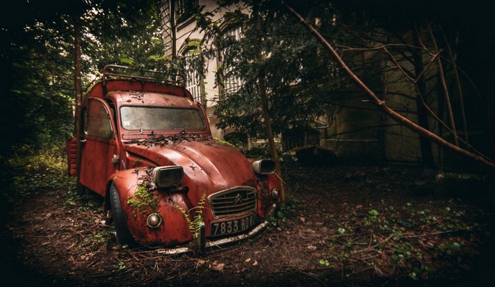 Abandoned red Citroën 2CV car in overgrown forest