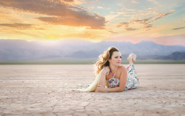 Woman lying on cracked earth at sunset