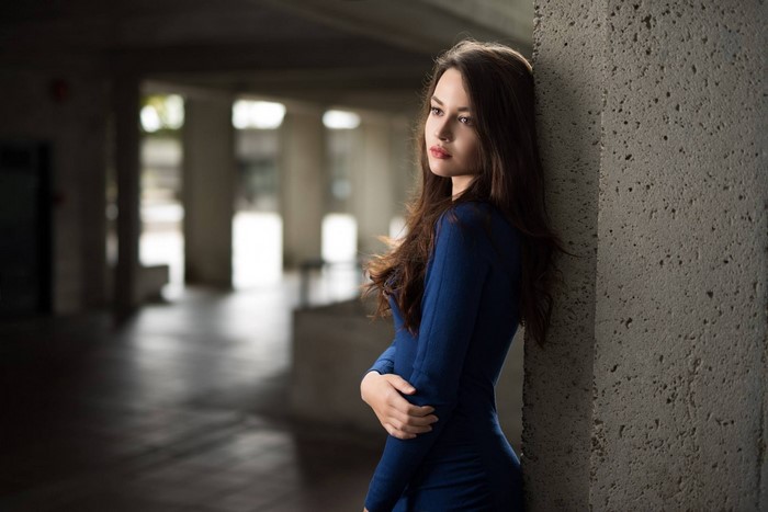 Woman in blue dress leaning against concrete pillar