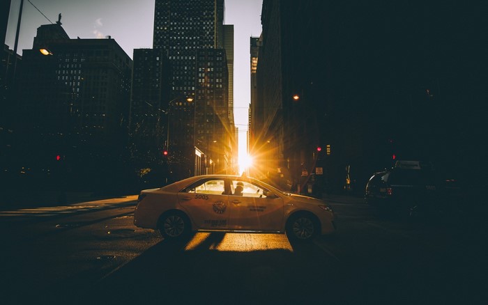 Yellow taxi driving through city street at sunset