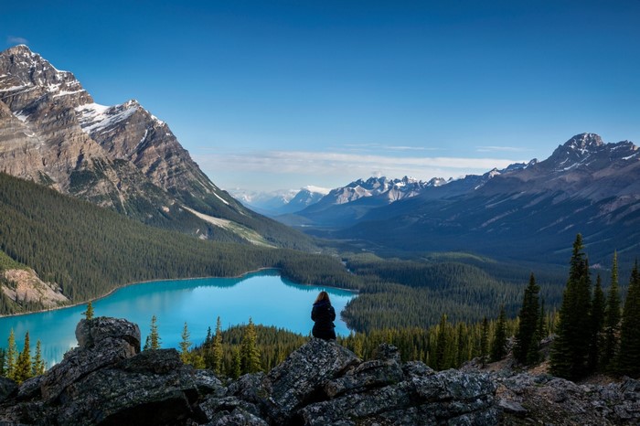 Woman sitting on rocks overlooking a turquoise lake and mountains