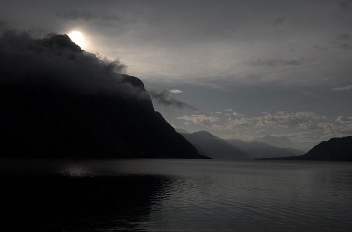 Sunlight breaking through clouds over a dark mountain and lake