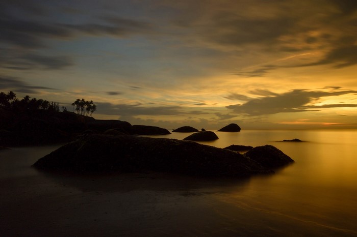Sunset over the ocean with rocks and palm trees