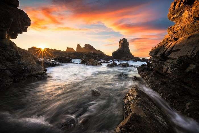 Rocky coast at sunset with sunburst over the ocean
