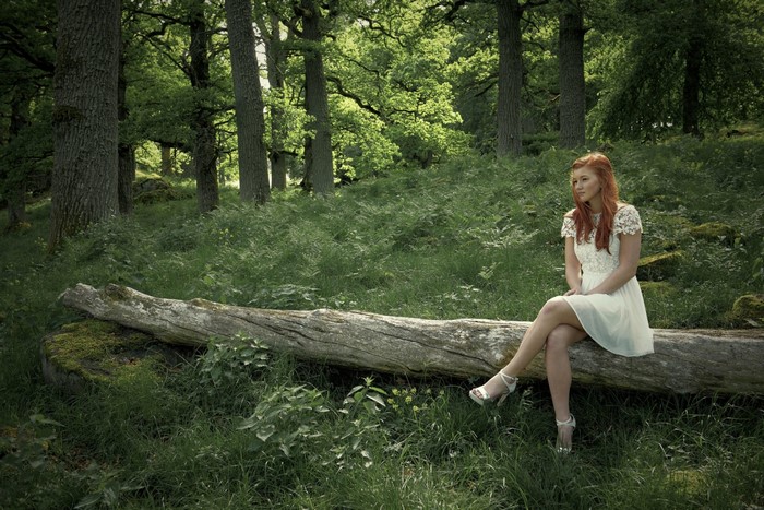 Woman in white dress sitting on a log in a forest