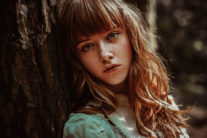 Girl with freckles leaning against a tree