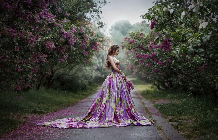 Woman in a floral dress holding flowers in a lilac garden