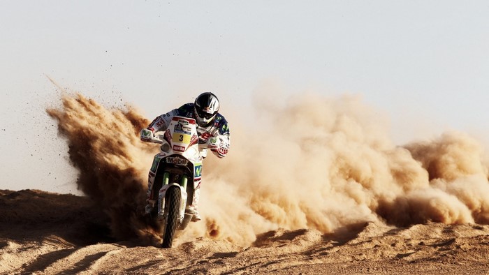 Motorcyclist racing through sand, kicking up dust