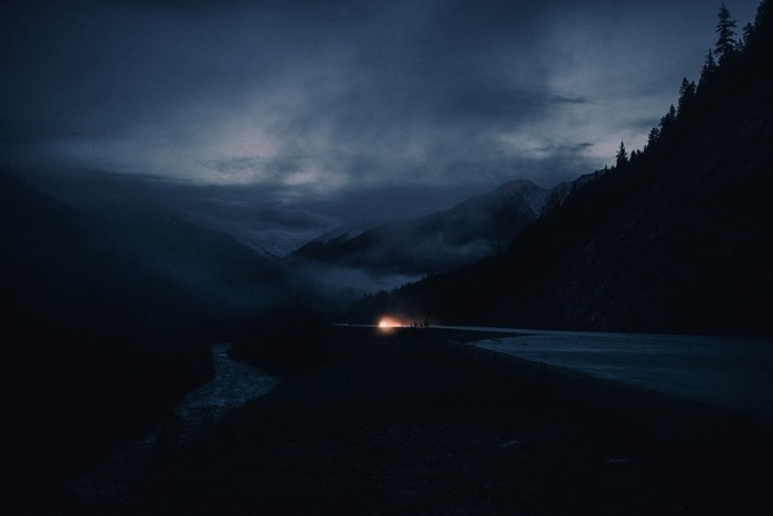 Car headlights illuminate a mountain road at dusk