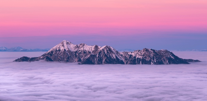 Snow-capped mountains above clouds at sunset