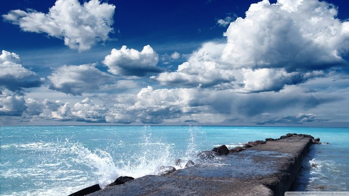 Concrete pier extending into a turquoise ocean under a cloudy sky