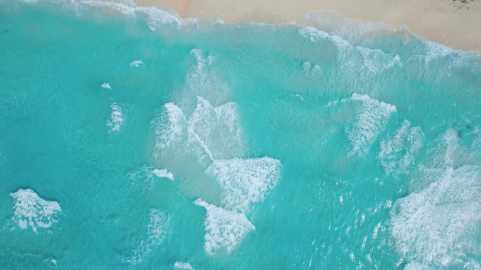 Aerial view of turquoise ocean waves crashing on a sandy beach