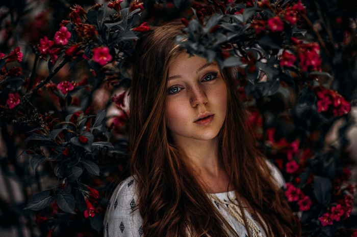Young woman with freckles surrounded by red flowers
