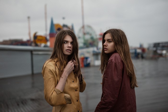 Two young women on a pier with amusement park in background