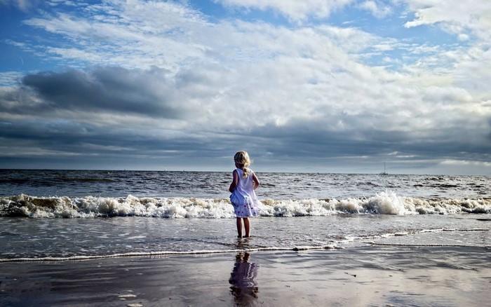 A young girl stands at the edge of the sea.
