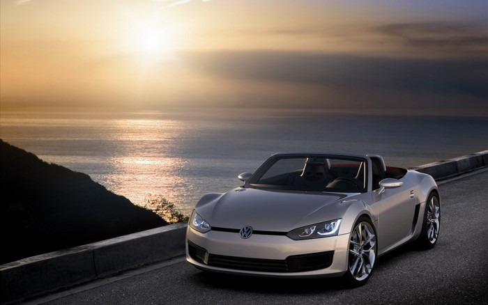 Silver Volkswagen convertible sports car on a coastal road at sunset
