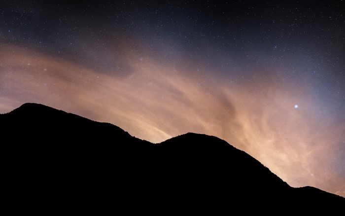 Silhouette of mountains against a starry night sky with clouds