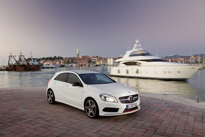 White Mercedes-Benz hatchback parked by a harbor with a yacht