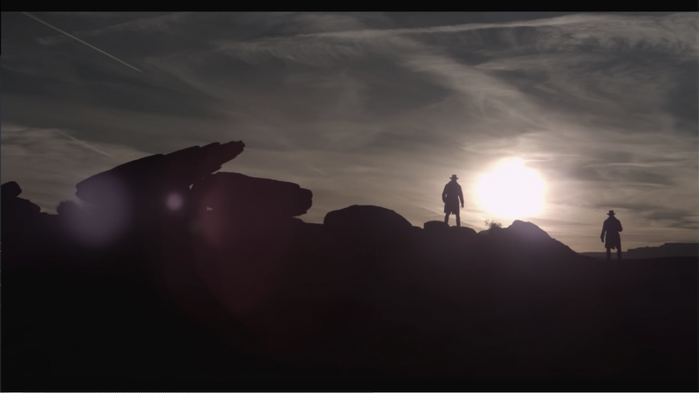 Two figures silhouetted against the sun at sunset
