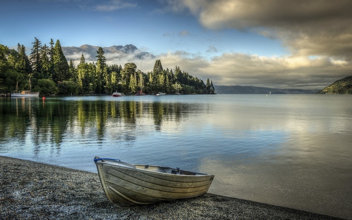 Boat on a pebble beach by a lake with trees and mountains