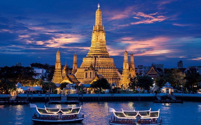Wat Arun temple at dusk with boats on the river in Bangkok, Thailand