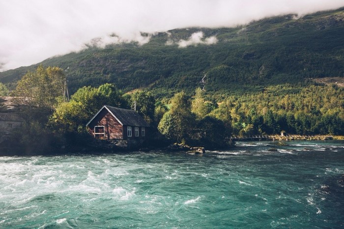 Wooden house by a river with mountains and forest