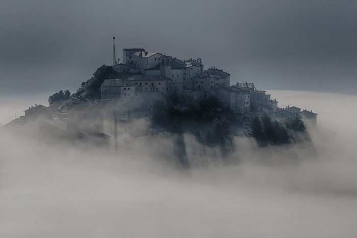 Village on a hill emerging from fog in Italy