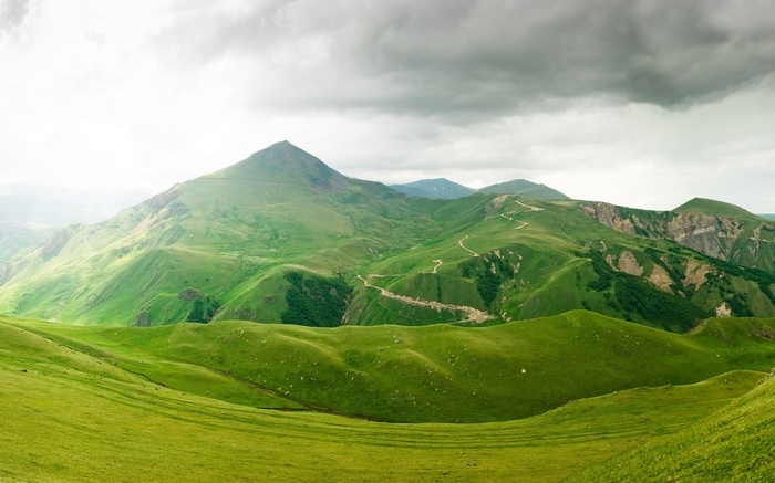 Green rolling hills and mountains under a cloudy sky