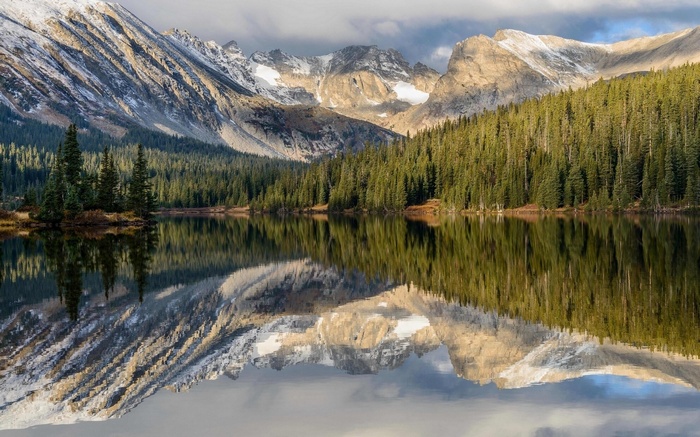 Mountain lake reflection with pine forest and snow-capped peaks
