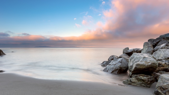 Ocean sunrise with pink clouds over water and rocks