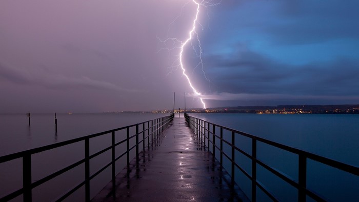 Lightning strikes over a pier and town at dusk