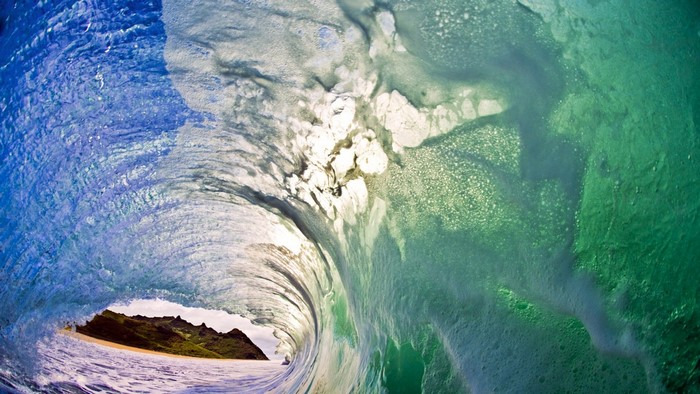 Inside a crashing ocean wave with a beach and mountains visible