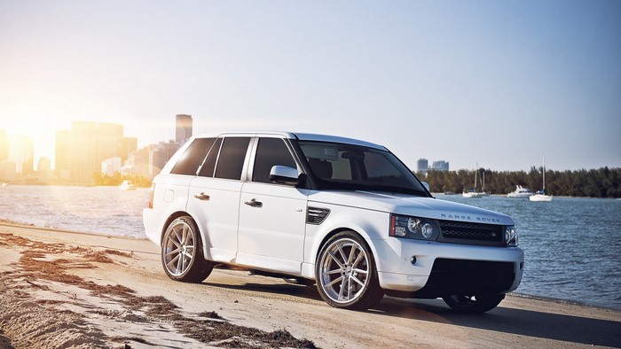 White Range Rover Sport on a beach with cityscape