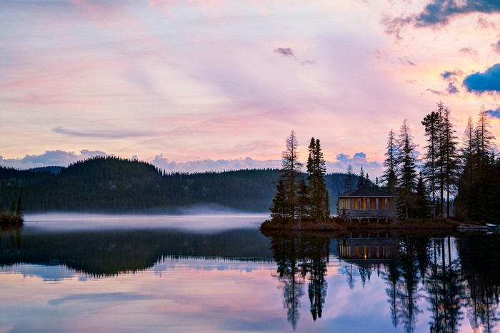 Cabin on an island in a misty lake at sunset