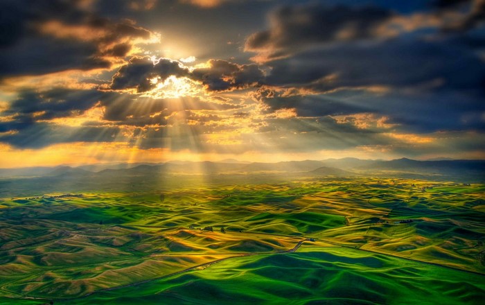 Sunlight Breaking Through Clouds Over Rolling Hills